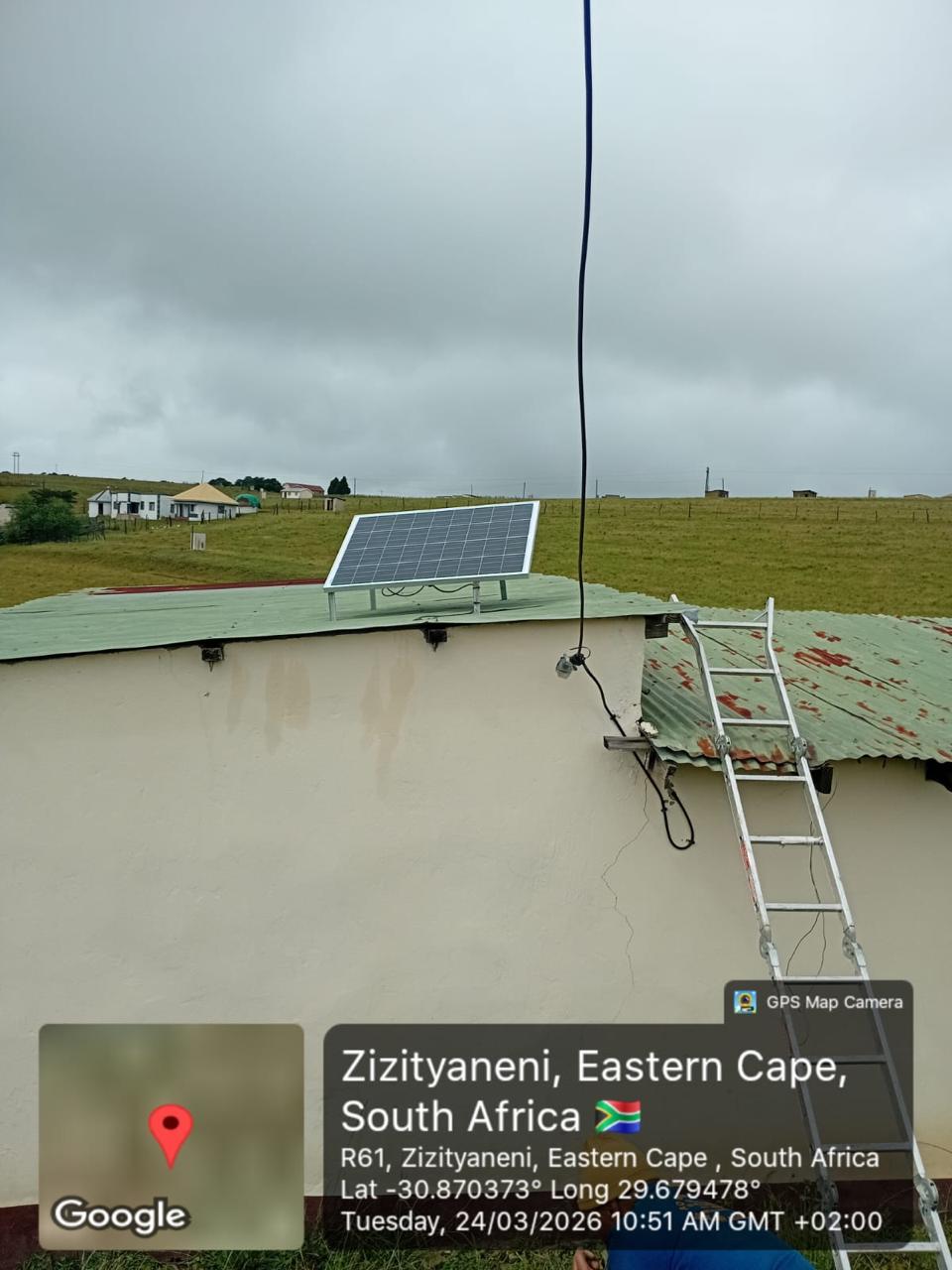 Rooftop solar panel with site surroundings visible in the background.
