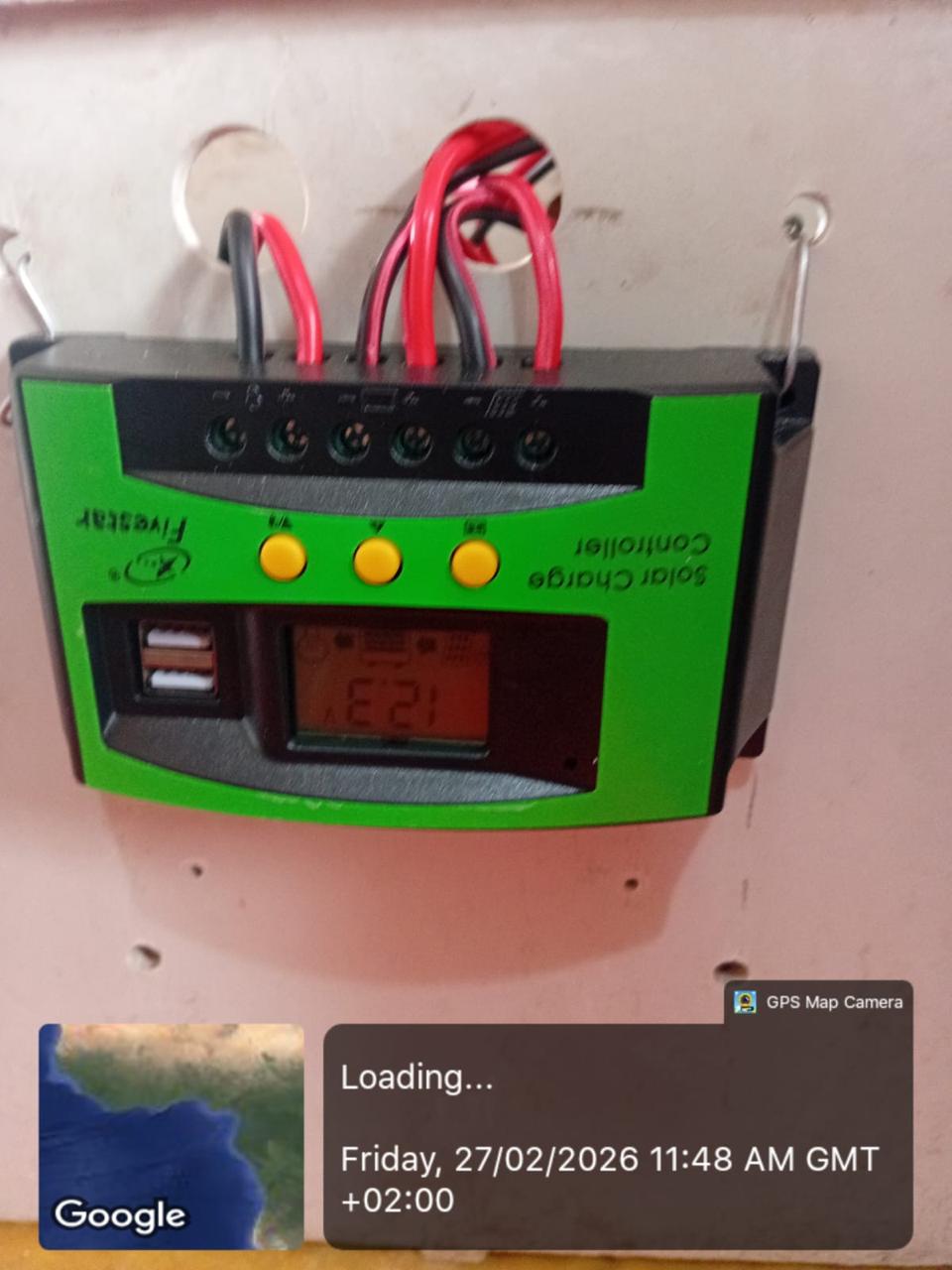 Wall-mounted solar charge controller with connected red and black wiring.